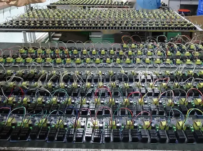 Rows of wired electronic circuit board assemblies arranged on production tables in a factory workshop