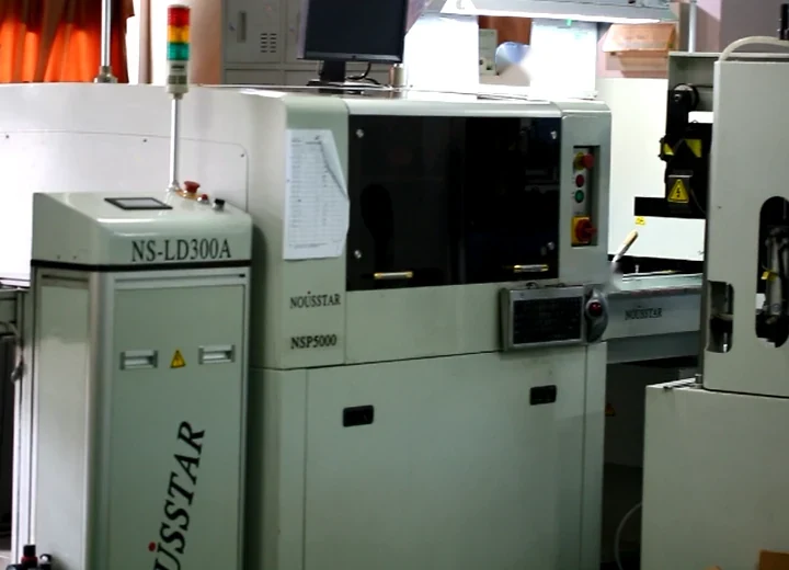 Industrial machinery in a factory setting, featuring a control cabinet and a main machine unit