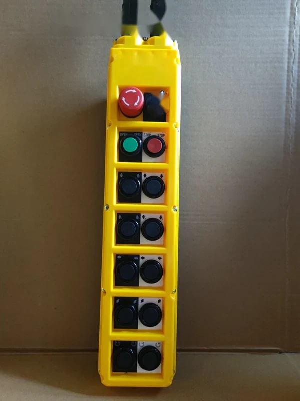 Yellow industrial pendant control station with red emergency stop, green and red buttons, and black pushbuttons