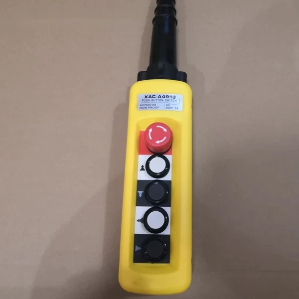 A yellow industrial pendant control station with a red emergency stop button and four black push buttons