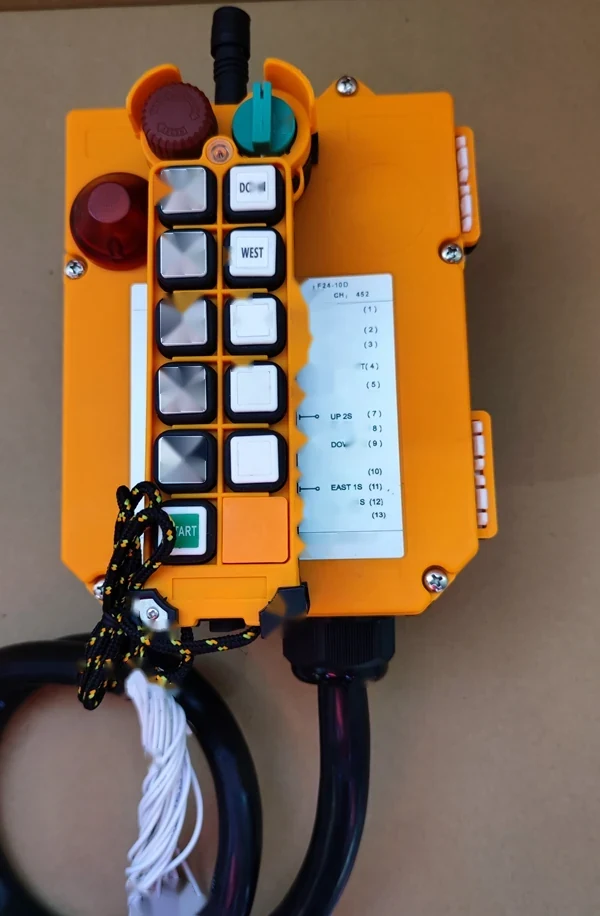 Orange industrial radio remote control with push buttons, emergency stop knob, key switch and attached cables