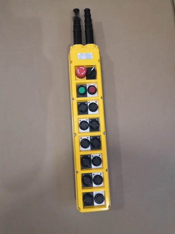 Yellow industrial pendant control station with red emergency stop, green button, and rows of black push buttons on beige surface