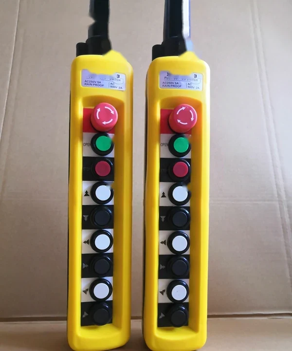 Two yellow industrial pendant control stations with red emergency stop buttons and push buttons