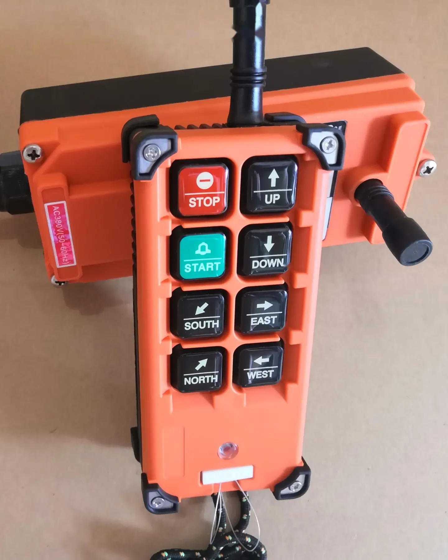 Orange industrial radio remote control with STOP, START and directional buttons and antenna, on a receiver unit