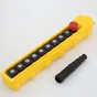 Yellow industrial pendant control station with push buttons and red emergency stop, black cable boot beside it