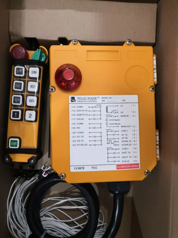 Yellow industrial radio remote control transmitter and receiver unit with a red emergency stop button and attached coiled cables