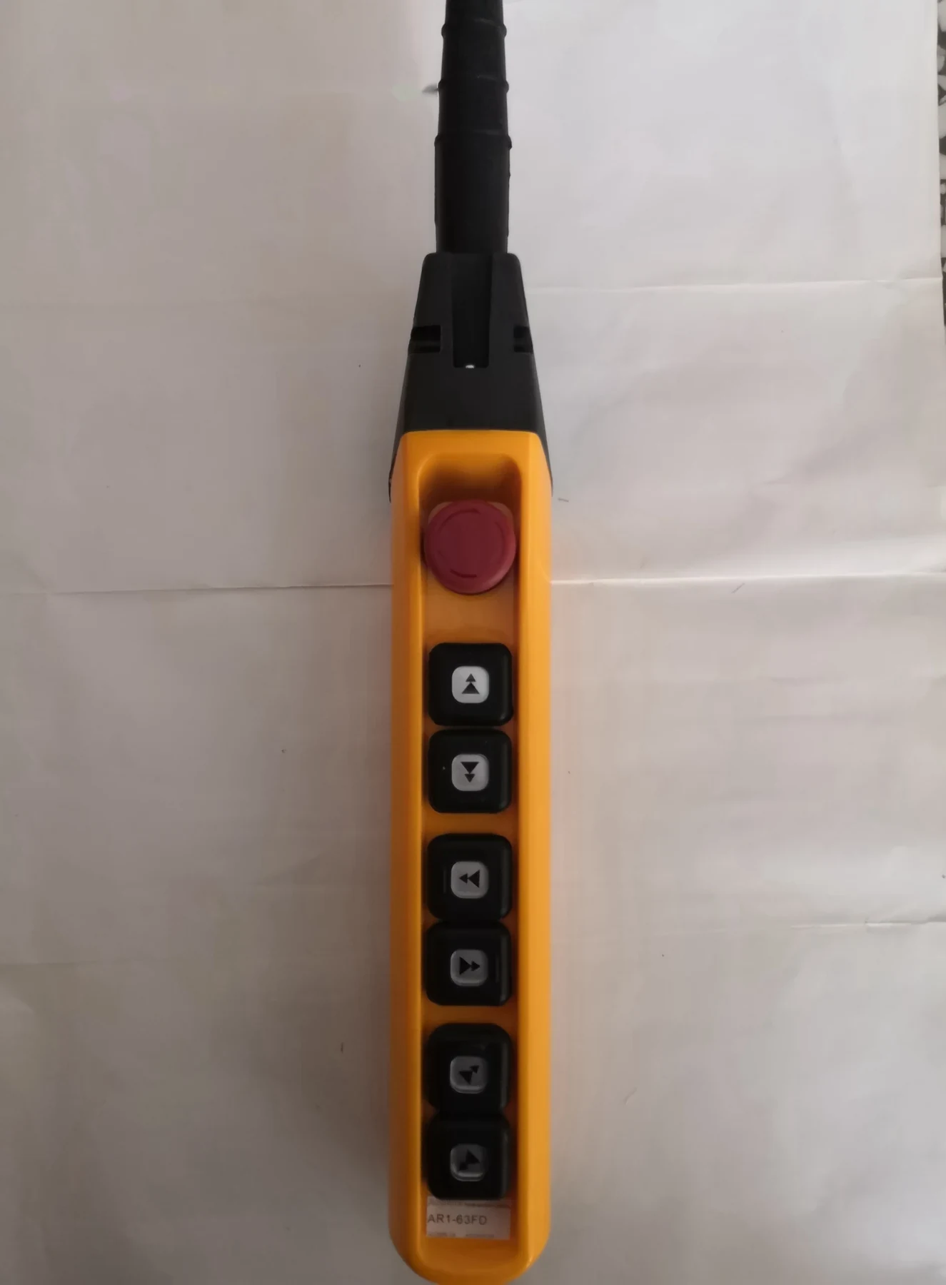 Yellow industrial pendant control station with red emergency stop button and black arrow push buttons on cable