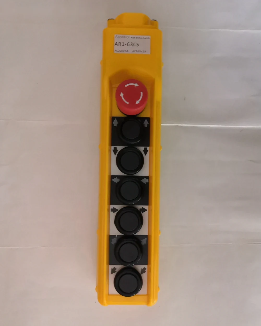 Yellow industrial pendant control station with red emergency stop knob and six black push buttons