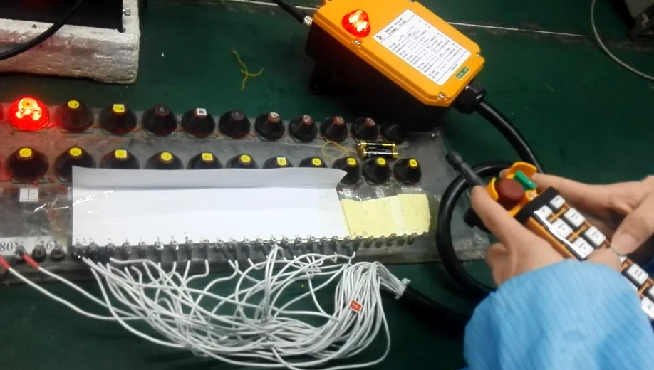 A worker's hands operate a yellow industrial pendant control station on a workbench