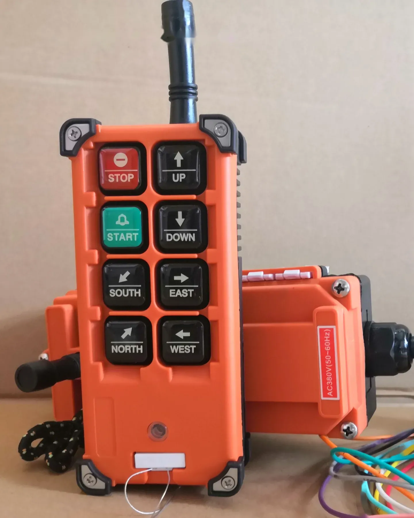 Orange industrial remote control with buttons for stop, start, up, down, and directional movement, with a receiver unit
