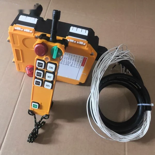 Yellow industrial crane radio remote control: handheld transmitter with direction buttons and red stop knob beside yellow receiver unit with coiled black cable and wires