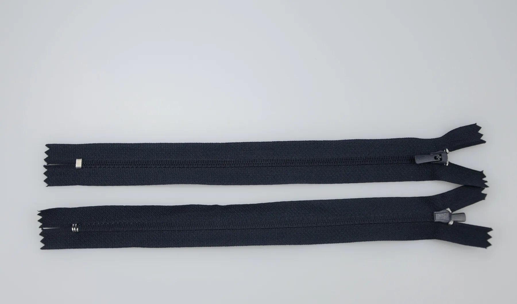 Two black zippers with metal sliders laid horizontally on a white background.