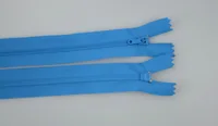 Two blue coil zippers with sliders laid diagonally on a plain light gray background
