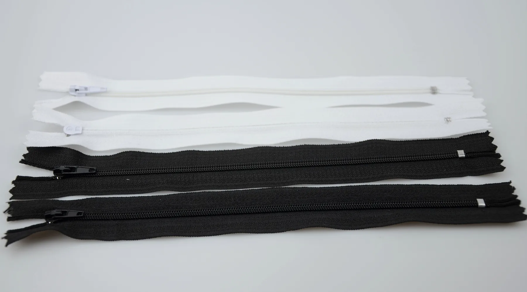 Several white and black zippers with sliders laid flat on a white surface