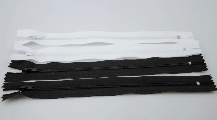 Several white and black zippers with sliders laid flat on a white surface