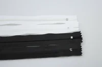 White and black closed-end zippers with sliders lying on a white surface