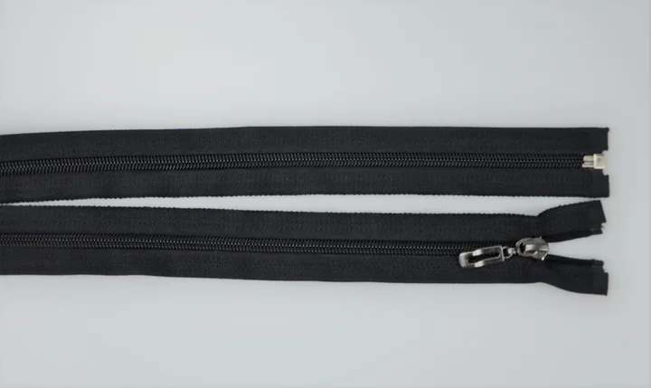 Two black coil zippers on a light gray surface, one with a metal slider and pull, the other detached at one end