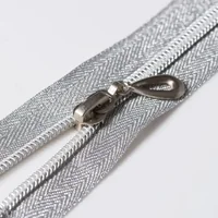 Close-up of a silver metallic zipper with slider and teardrop pull tab on white herringbone fabric