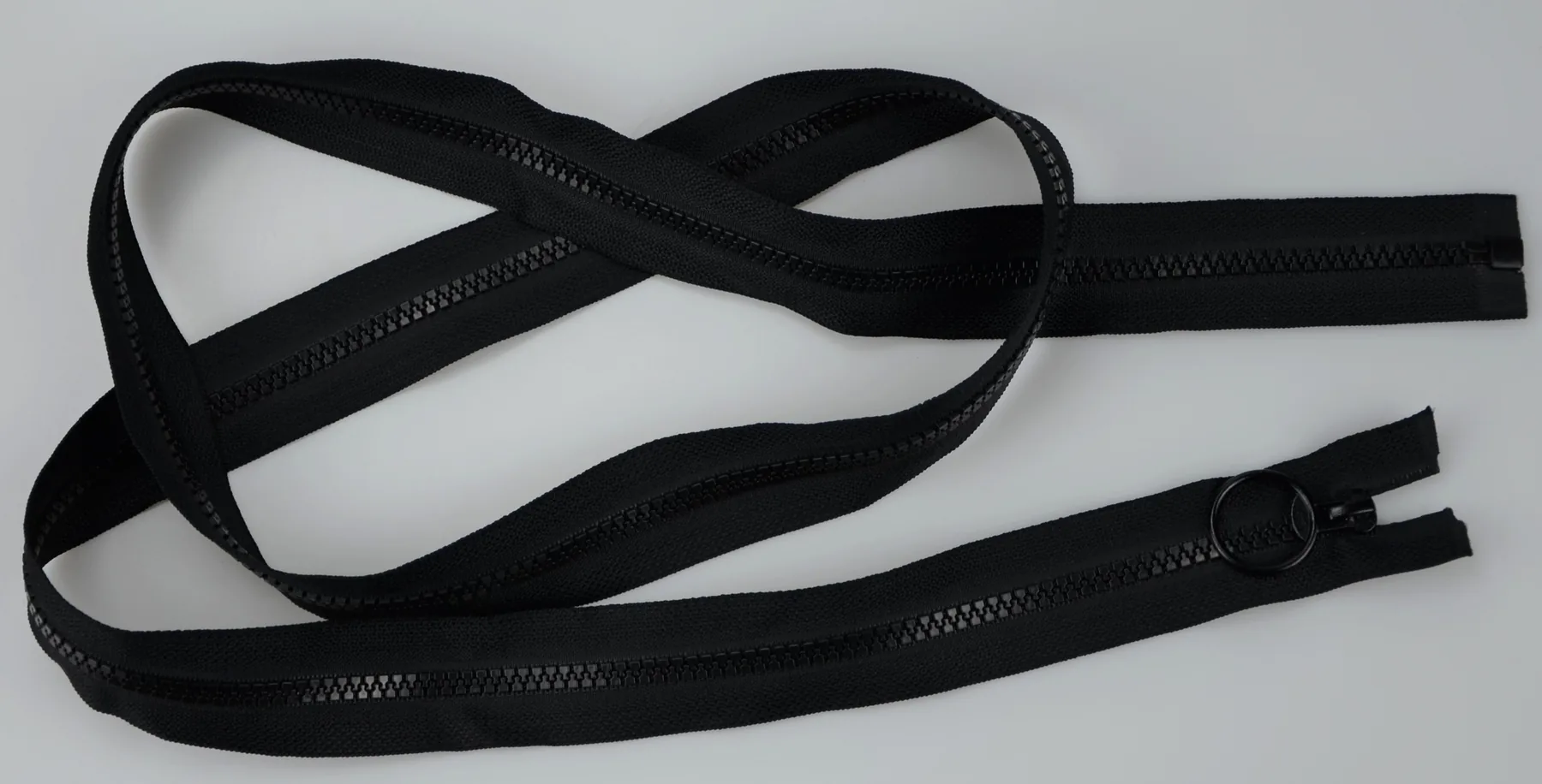 Coiled black zippers with pull tabs laid loosely on a plain light gray background