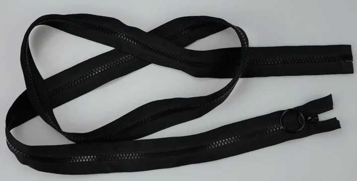 Coiled black zippers with pull tabs laid loosely on a plain light gray background