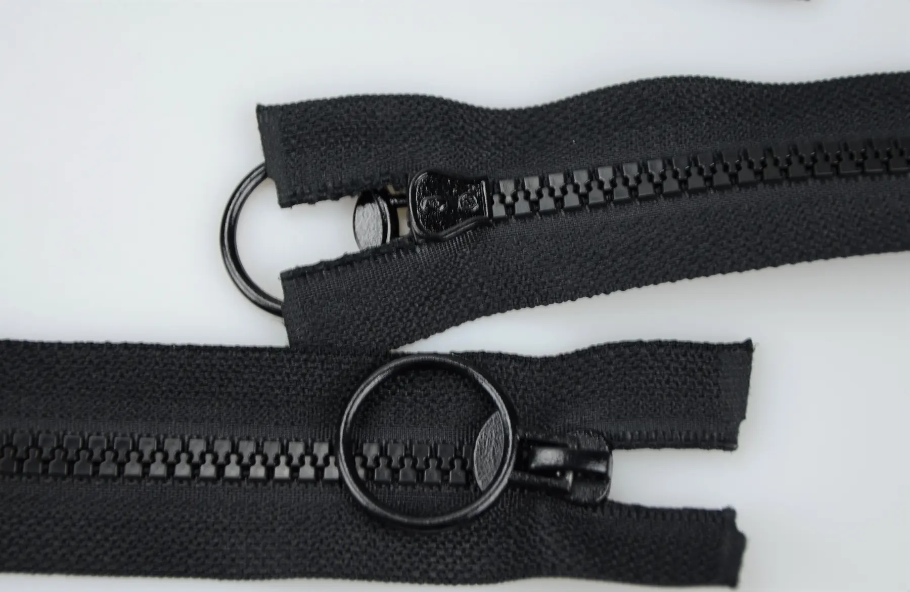 Two black zippers with large round O-ring pullers laid on a white background