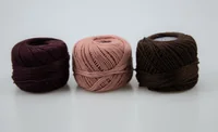Three balls of yarn in dark burgundy, pink, and dark brown arranged side by side on