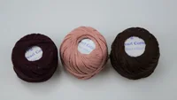 Three balls of pearl cotton embroidery thread in dark burgundy, pink, and dark brown on a plain white background