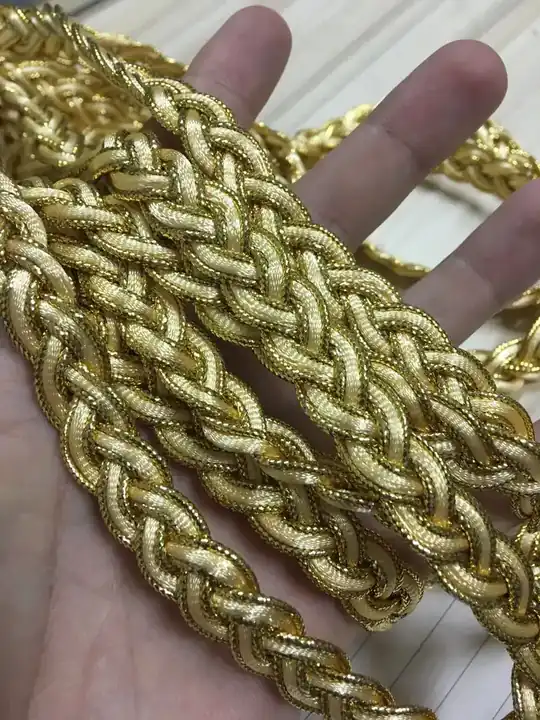 Hand holding coiled golden metallic braided cord trim over a wooden surface