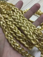 Hand holding coiled golden metallic braided cord trim over a wooden surface