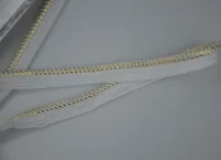 White woven braid trim with gold metallic thread lying crossed on a plain gray surface