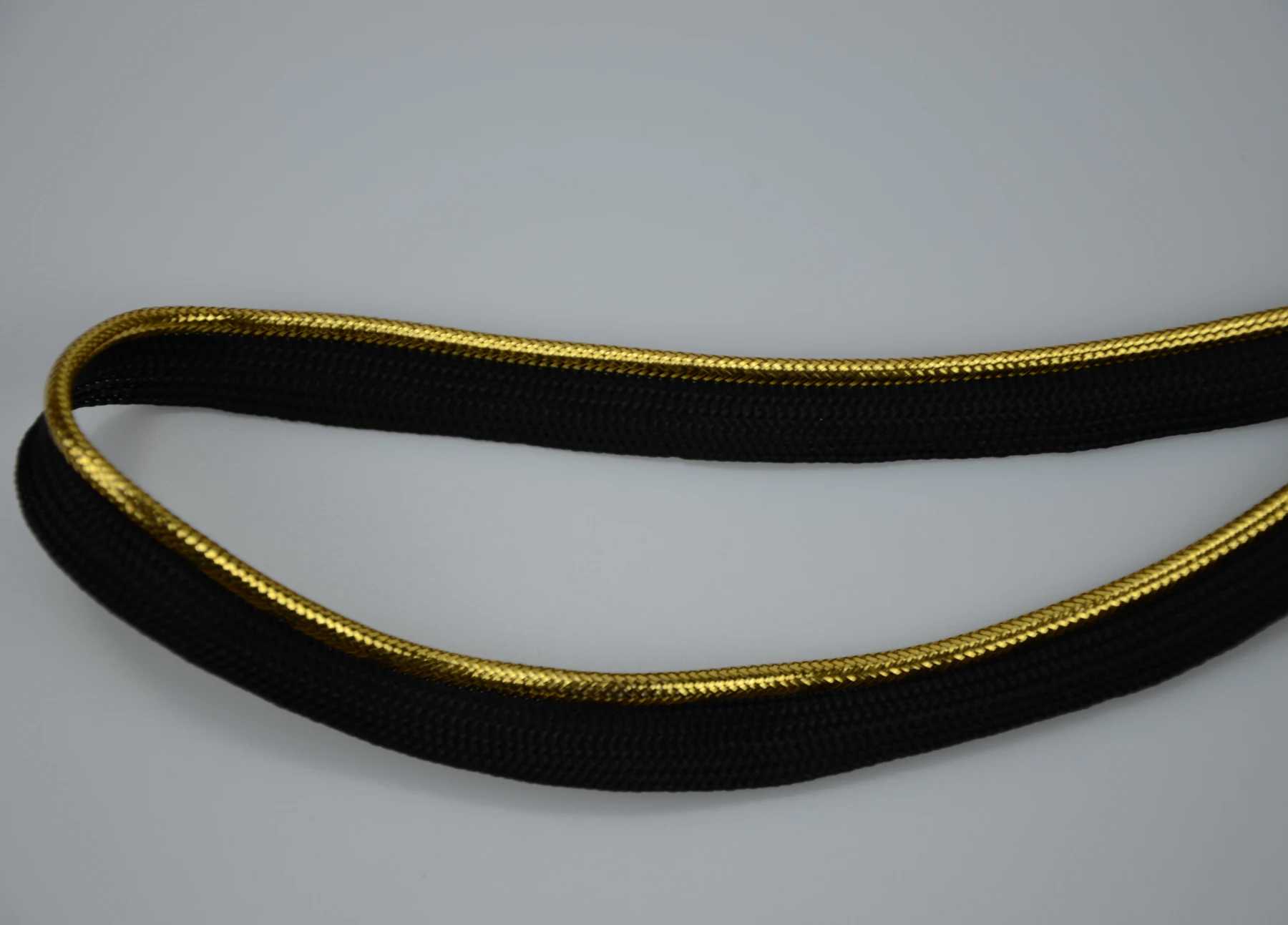 Coiled black woven trim with a metallic gold stripe along its edge on a plain background