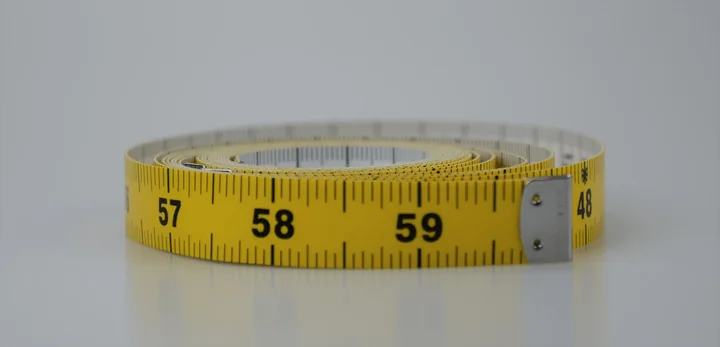 Coiled yellow tailor's measuring tape with visible markings around 57-59 centimeters on a white background
