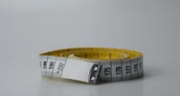 Yellow tailor's measuring tape coiled with printed centimetre markings on a plain gray background
