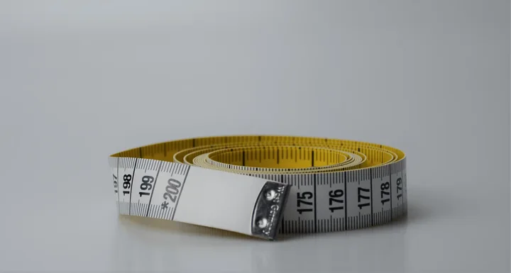 Coiled yellow tailor's measuring tape with printed numbers on a plain grey background