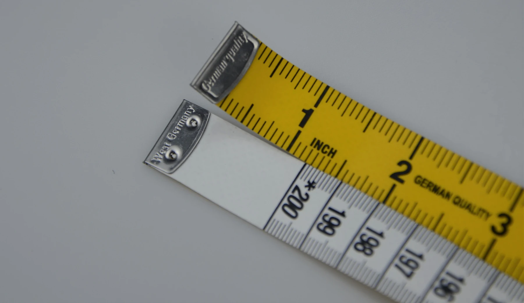 Yellow and white measuring tapes with metal end pieces on a gray background