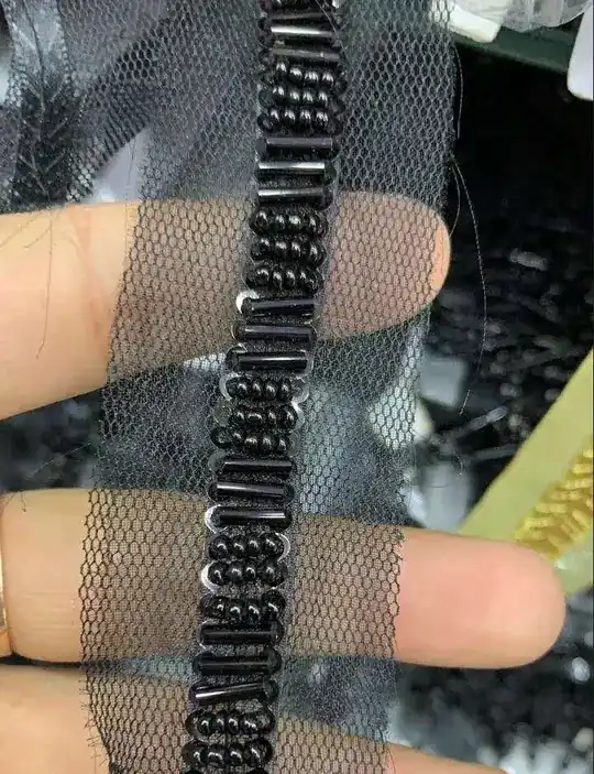 Black bugle and seed bead embroidered trim on tulle mesh held between fingers
