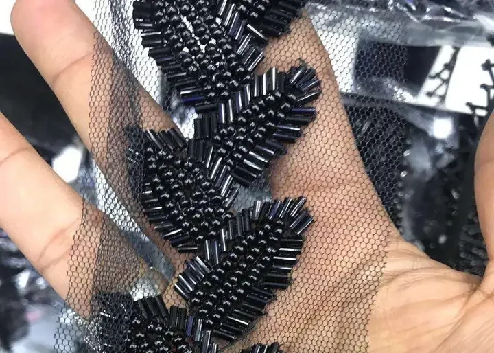 Hand holding black bugle-bead leaf motif beaded trim on tulle mesh fabric