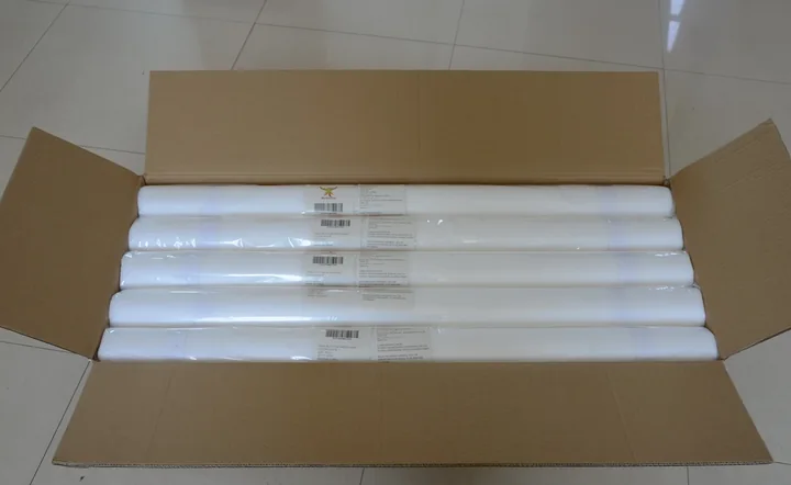 Open cardboard box containing five white rolled products with small labels, on a tiled floor