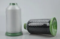 Two large spools of sewing thread, one white upright and one black lying on its side, wrapped in green mesh netting