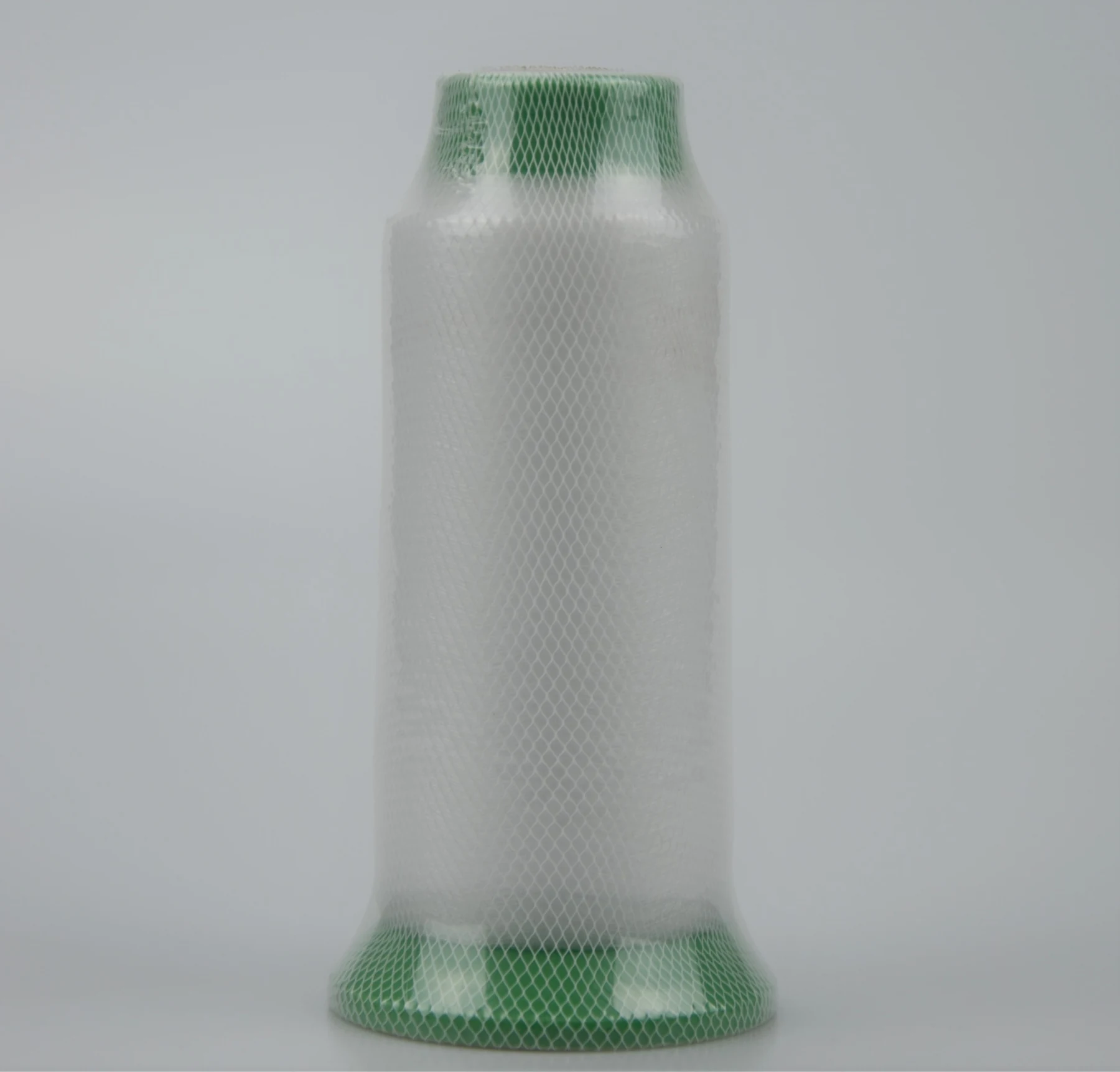Large spool of white thread wrapped in green mesh netting on a plain gray background