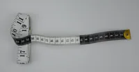 White tailor's measuring tape with black numbered markings coiled on a plain grey background