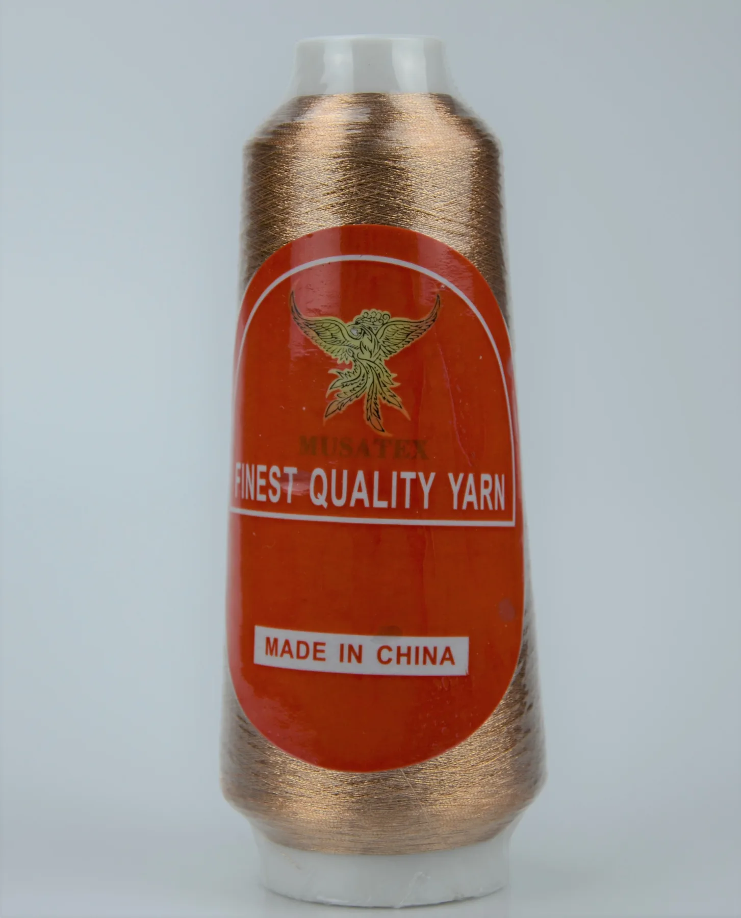 Copper metallic yarn cone with orange MUSATEX label reading FINEST QUALITY YARN and MADE IN CHINA