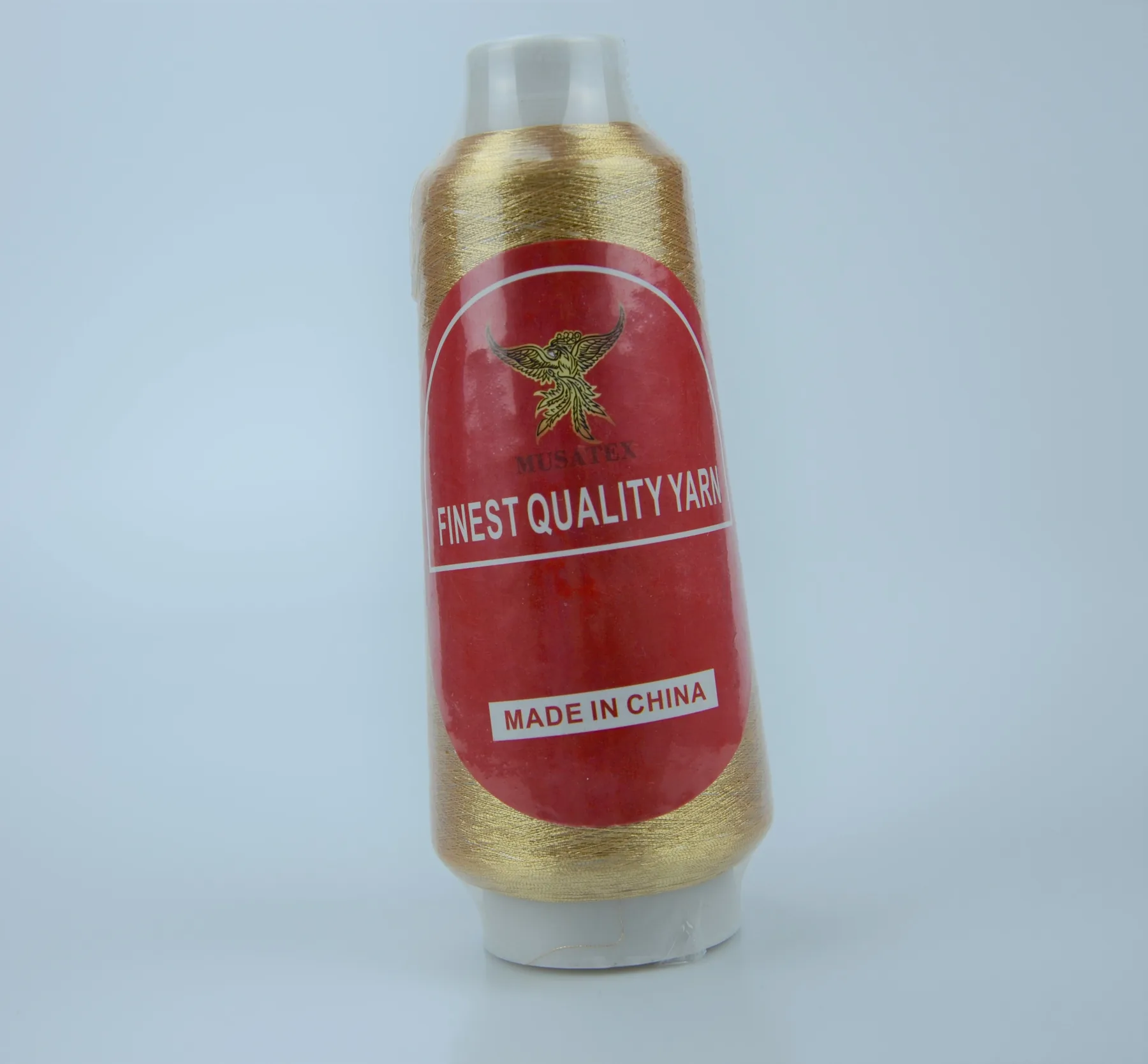 A gold thread cone with a red MUSATEX label on a white background.