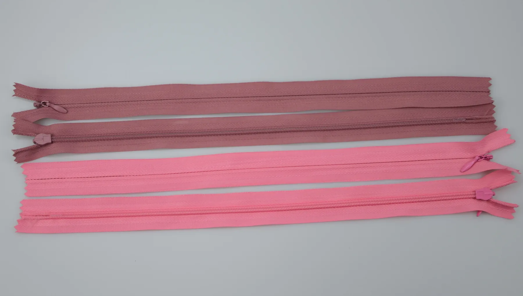 Four pink and mauve closed-end zippers with pull sliders arranged horizontally on a plain light background.