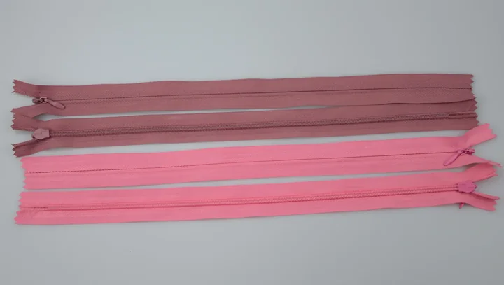 Four pink and mauve closed-end zippers with pull sliders arranged horizontally on a plain light background.