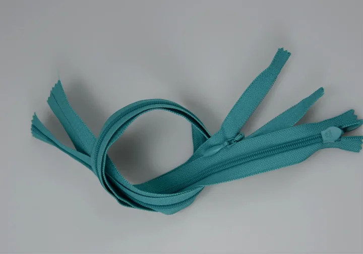 Several teal nylon zippers loosely coiled on a plain light background