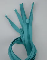 Several teal nylon zippers with sliders arranged in a fan shape on a plain light background