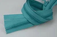 Close-up of teal nylon zippers coiled on a plain light background