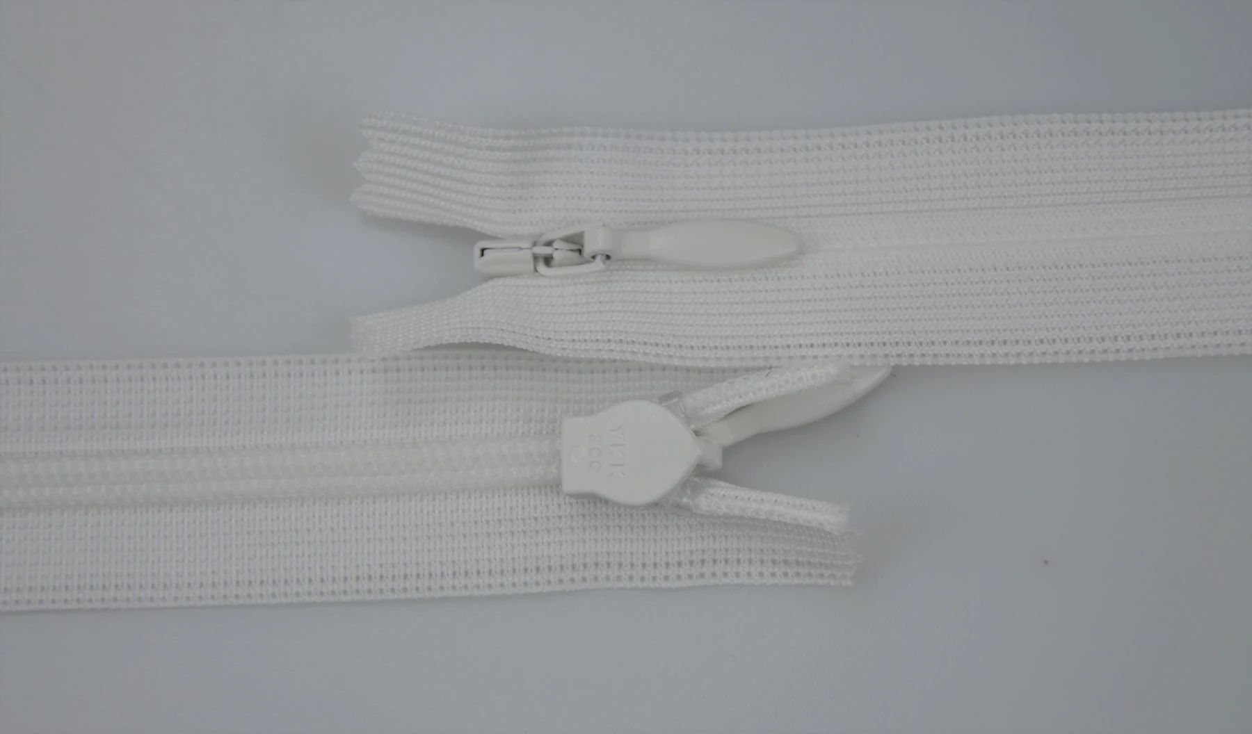 Two white nylon coil zippers with metal and plastic sliders on a plain light background