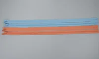 Blue and orange nylon zippers laid horizontally on a plain light gray background